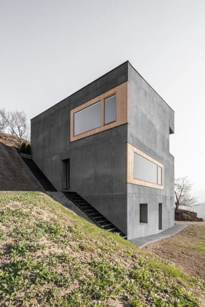 Casa em declive: fachada de concreto aparente com janela de madeira (projeto: Andreas Gruber)