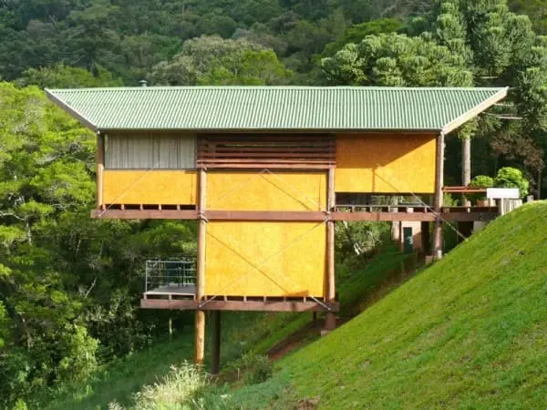 Casa em declive: cabana com fachada amarela e telhado verde (projeto: André Eisenlohr + Cabana Arquitetos)