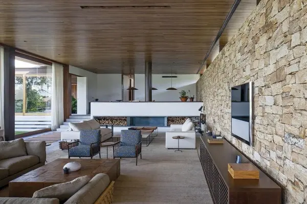 Tendências de Arquitetura e Design em 2021: sala de estar com parede de pedras, poltronas estampadas e sofá com tecido neutro (foto: Patricia Martinez)