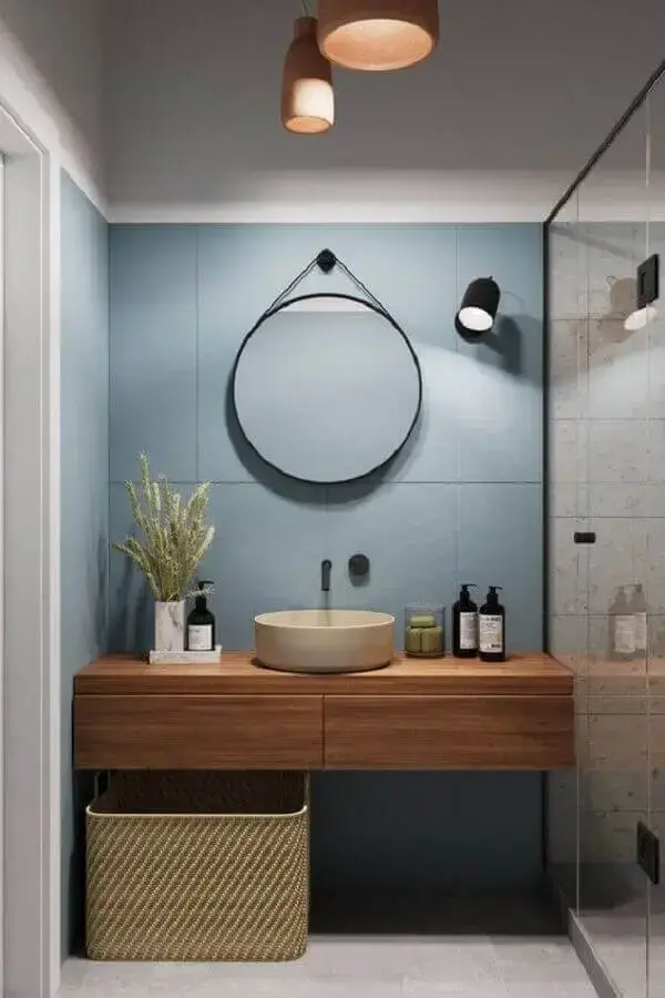 Luminária de banheiro de parede e bancada de madeira decoram o espaço