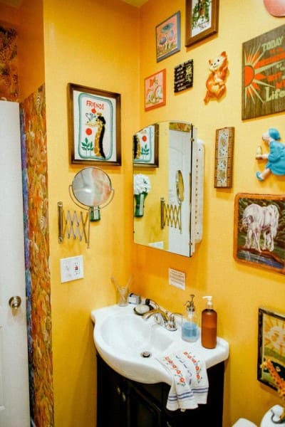 Kitsch: banheiro amarelo com quadros grandes (foto: The Everygirl)