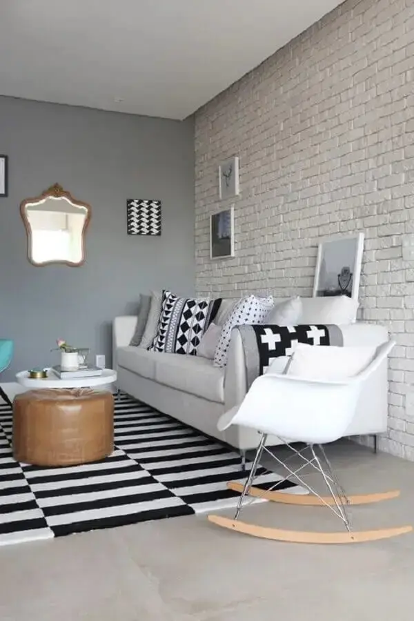 Parede de tijolo de gesso decora a sala de estar com tapete preto e branco e cadeira eames de balanço. Fonte: Futurist Architecture