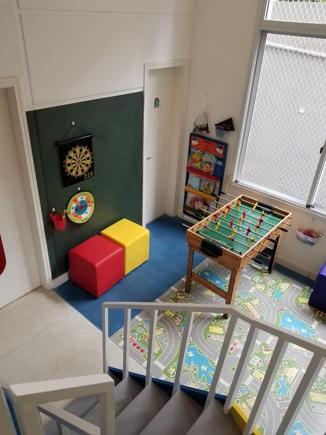 Sala de jogos com mesa de pebolim, parede de lousa verde e tapete temático infantil